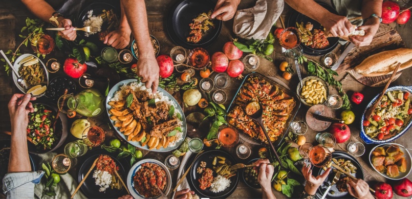 Array of healthy food on a table with people reaching for dishes. 