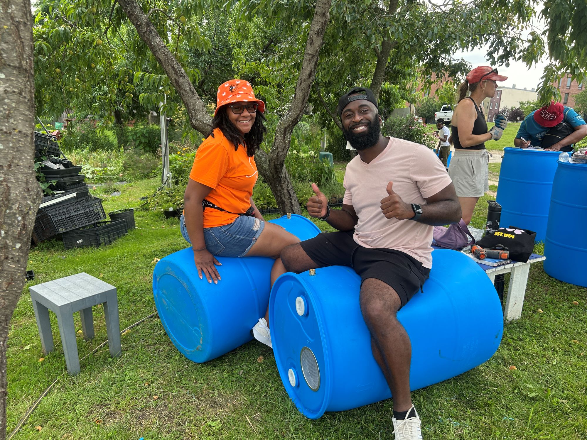 The image shows a two people sitting on blue barrels.
