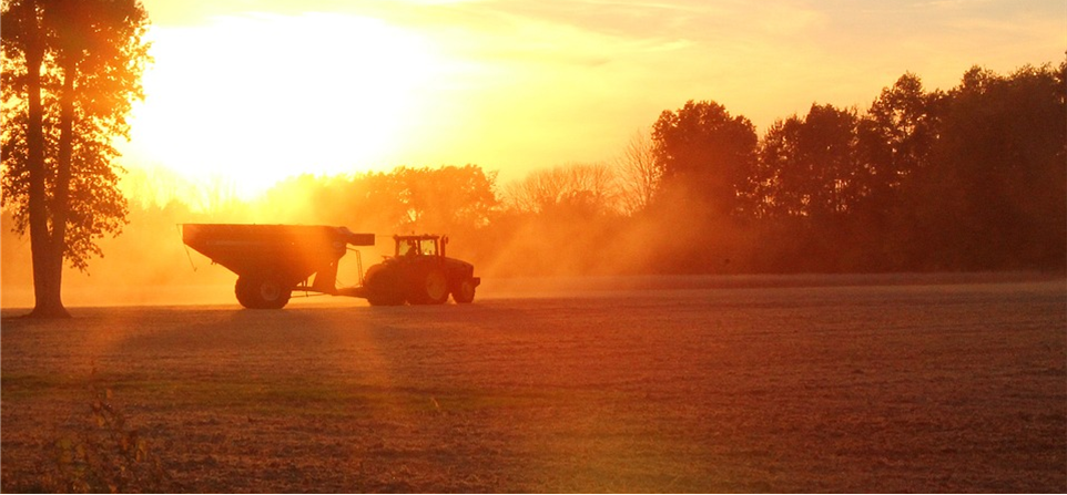 Sunrise over field with farm equipment in silhouette