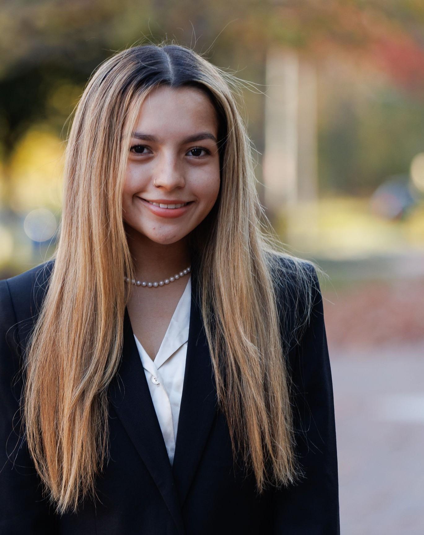 Smiling student dressed professionally set against colorful blurred background.