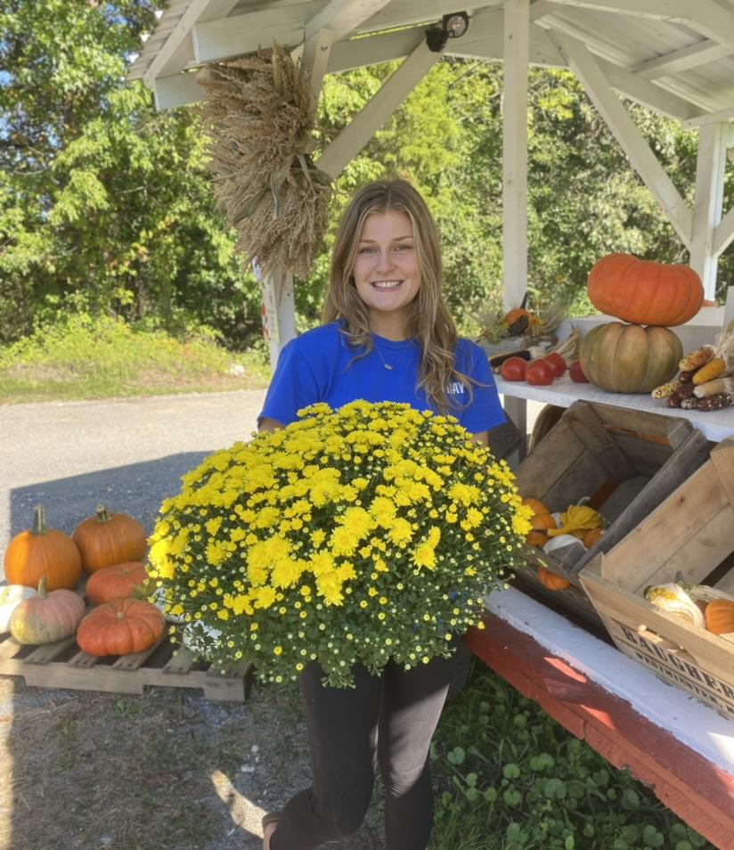 Smiling student at a farm stand holding vibrant yellow mums.