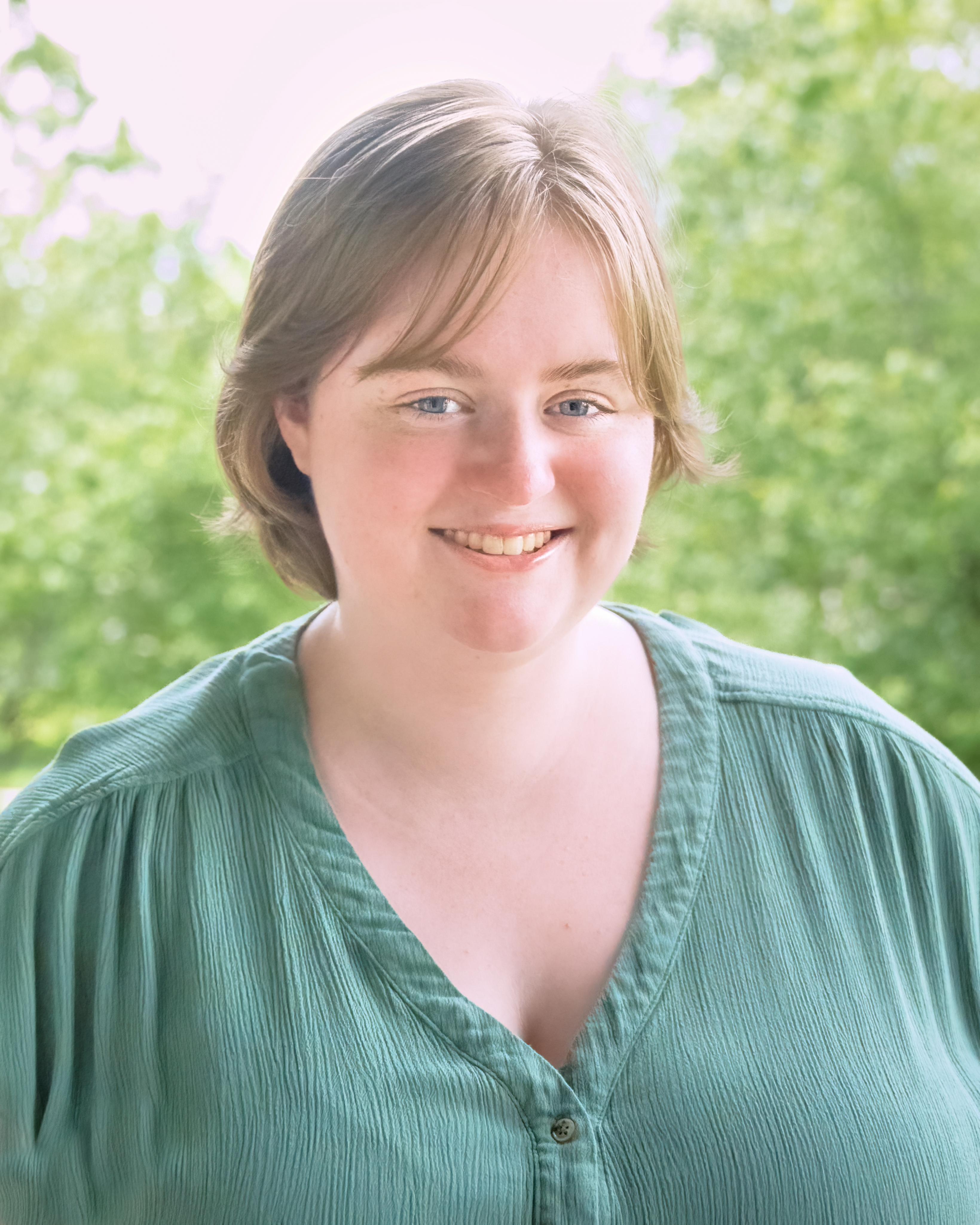 Smiling student in green surrounded by greenery.