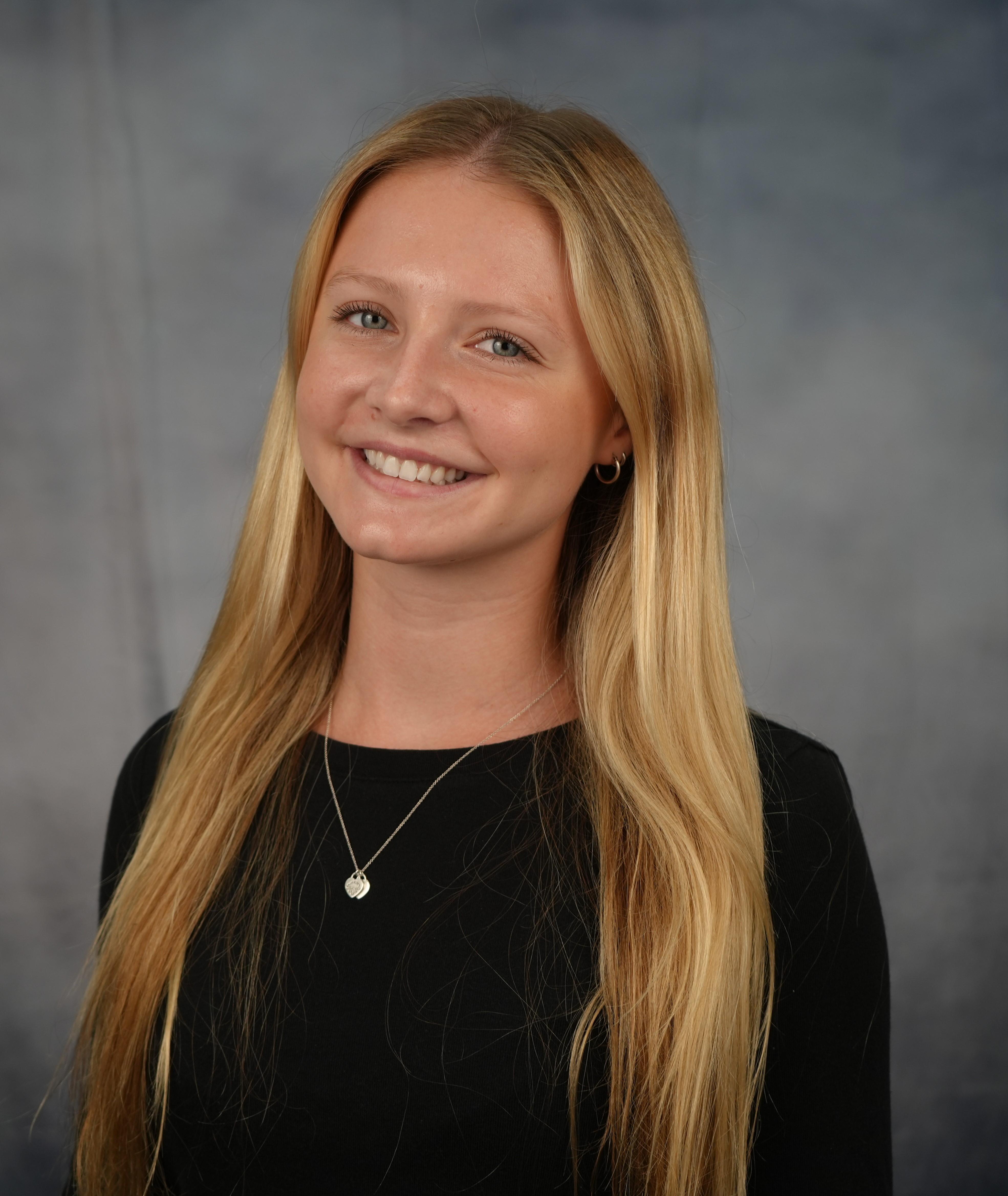 Smiling student in front of a traditional photography studio backdrop.