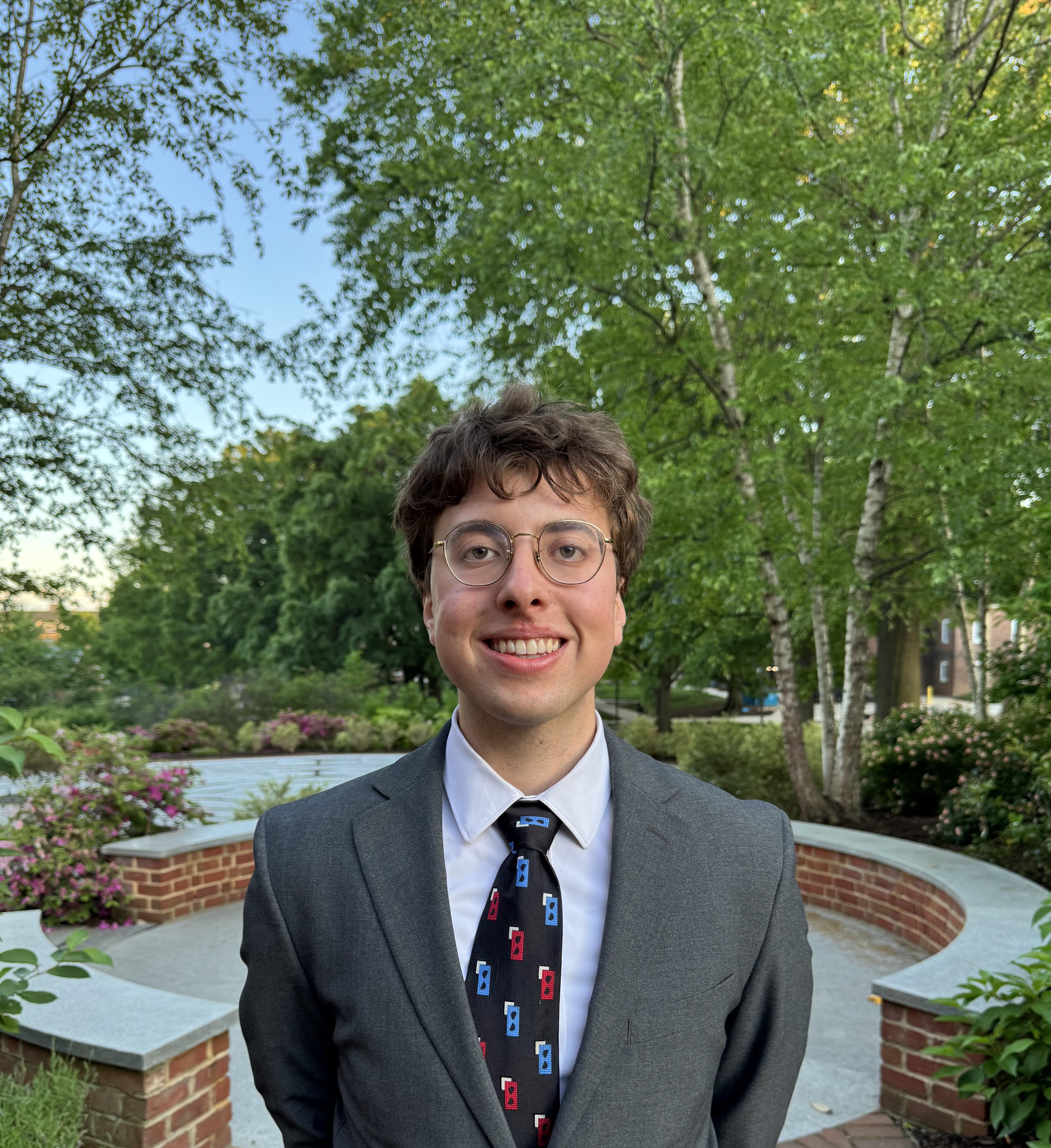 Suited student standing proudly in front of beautiful University of Maryland landscaping.