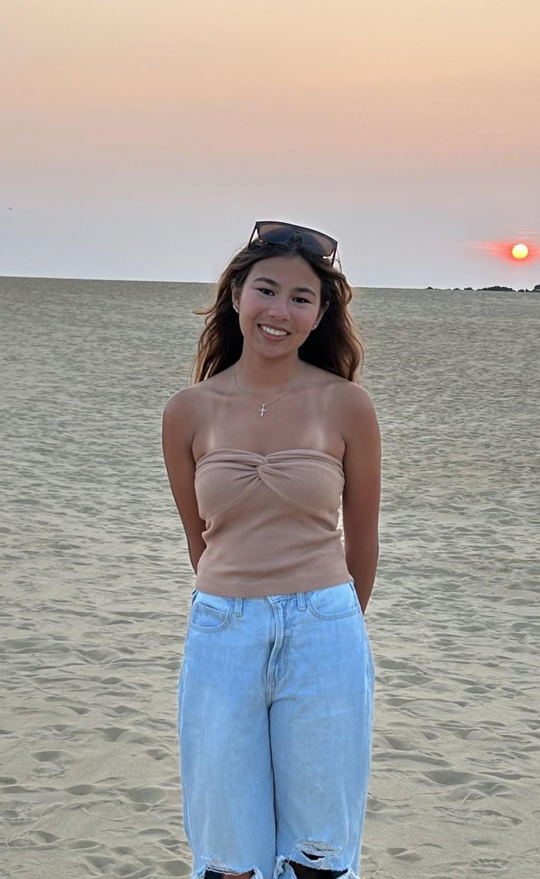 Student standing on a beach while the sun sits low in the background.