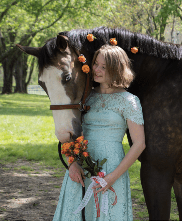 Formally dressed student posing with rose-studded horse.