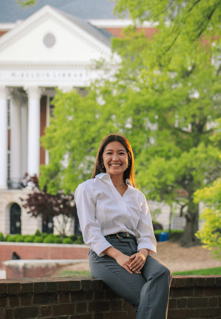 Professionally dressed student sitting cross-legged in the forefront with an iconic University of Maryland building in the background.