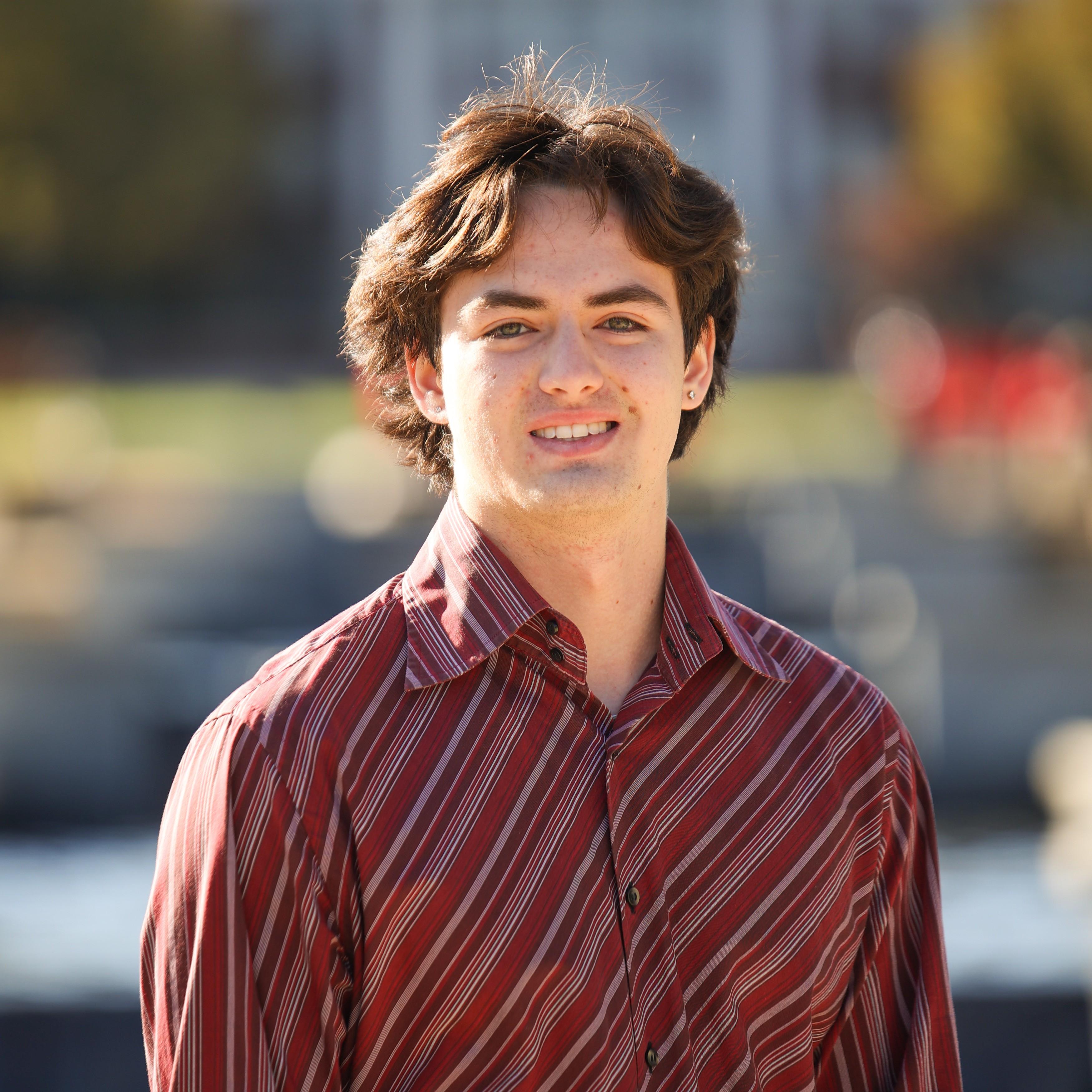 Mac is smiling at the camera, standing in front of the ODK Fountain on McKeldin Mall