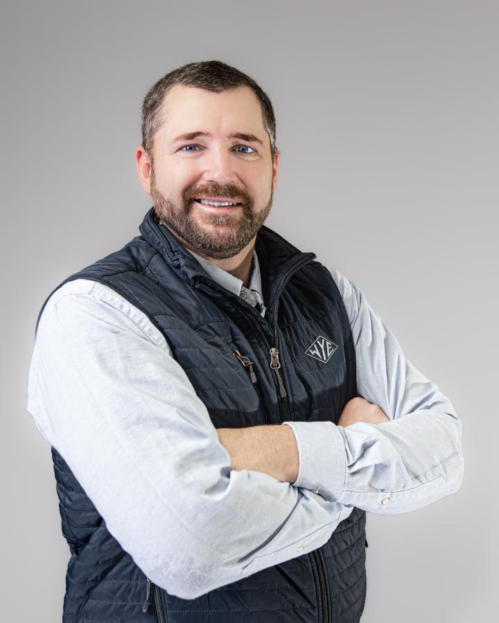 Heath McPherson stands for a portrait wearing a blue vest and light blue shirt.