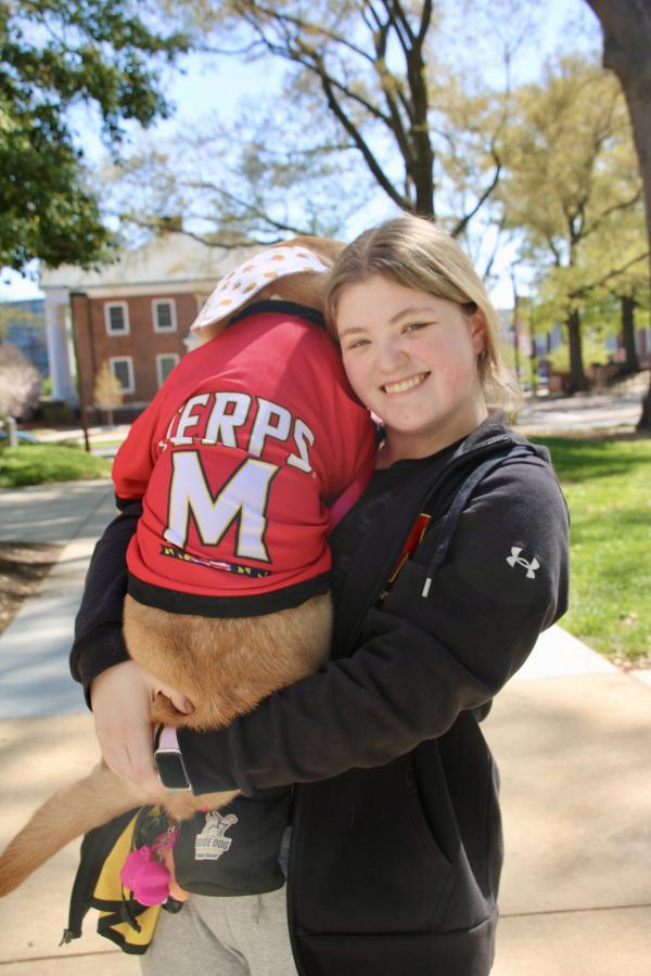Smiling student holds a yellow labrador who is wearing a University of Maryland Terps jersey! Go Terps.