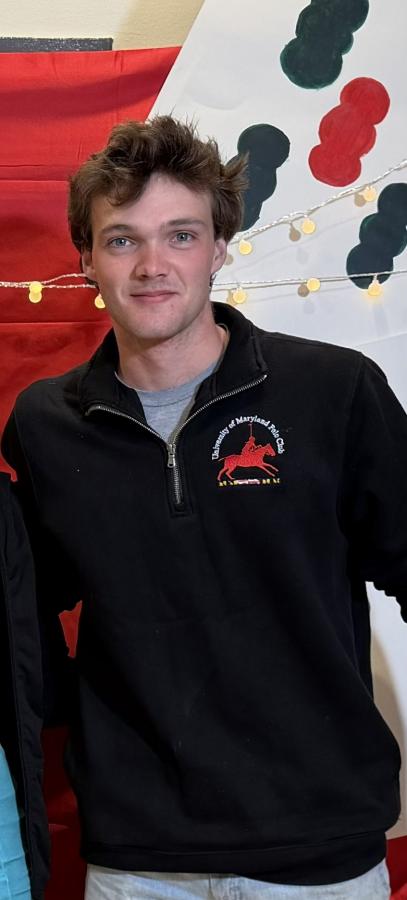 A student clad in a University of Maryland Polo Club quarter-zip stands proudly against the backdrop of UMD school colors.