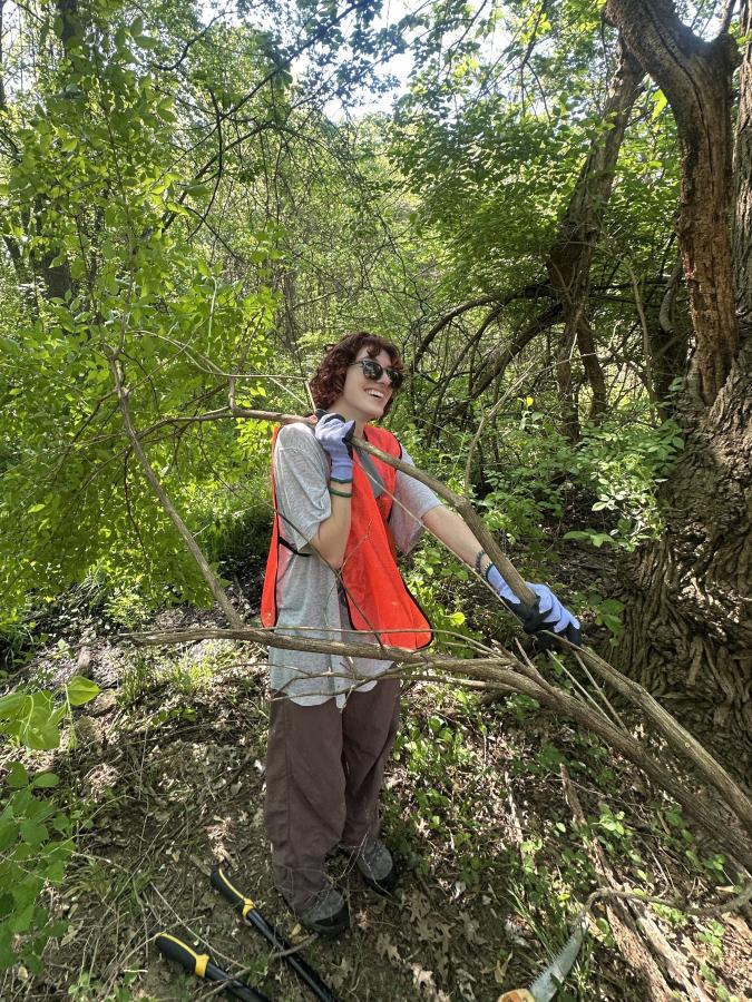 A student works happily in her orange safety vest, clearing fallen branches.