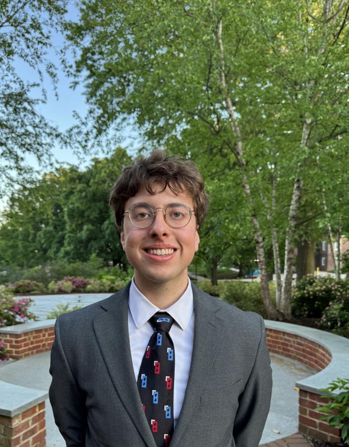 Suited student standing proudly in front of beautiful University of Maryland landscaping.
