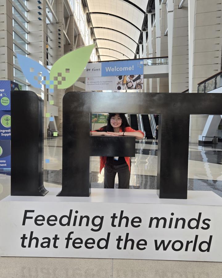 Student proudly stands against large letters representing the professional organization she participates in, the Institute of Food Technologists.