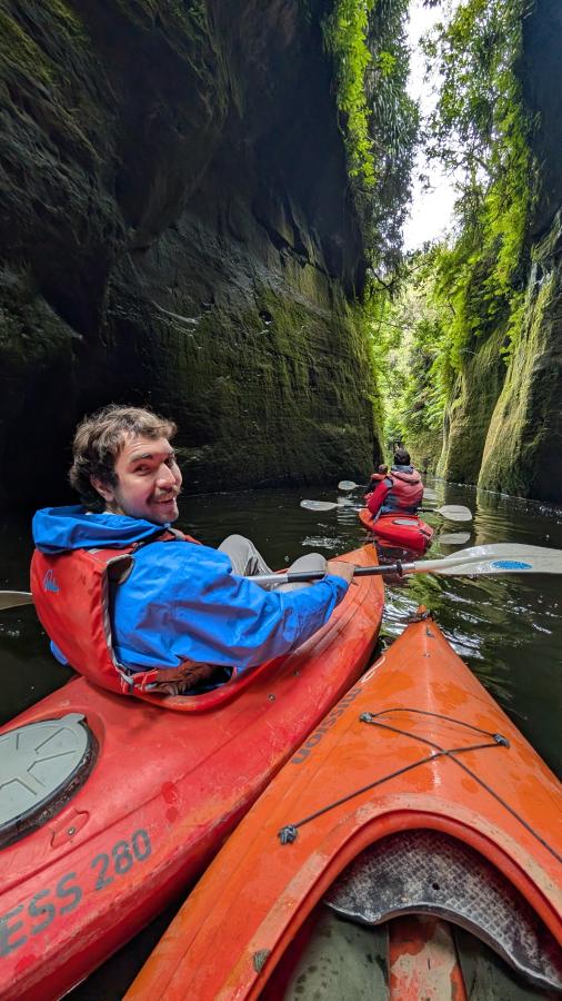 A student looks back at the photographer while paddling a bright red kayak through river gorge.