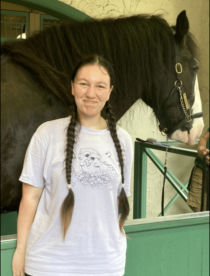 A student stands happily in front of her horse.