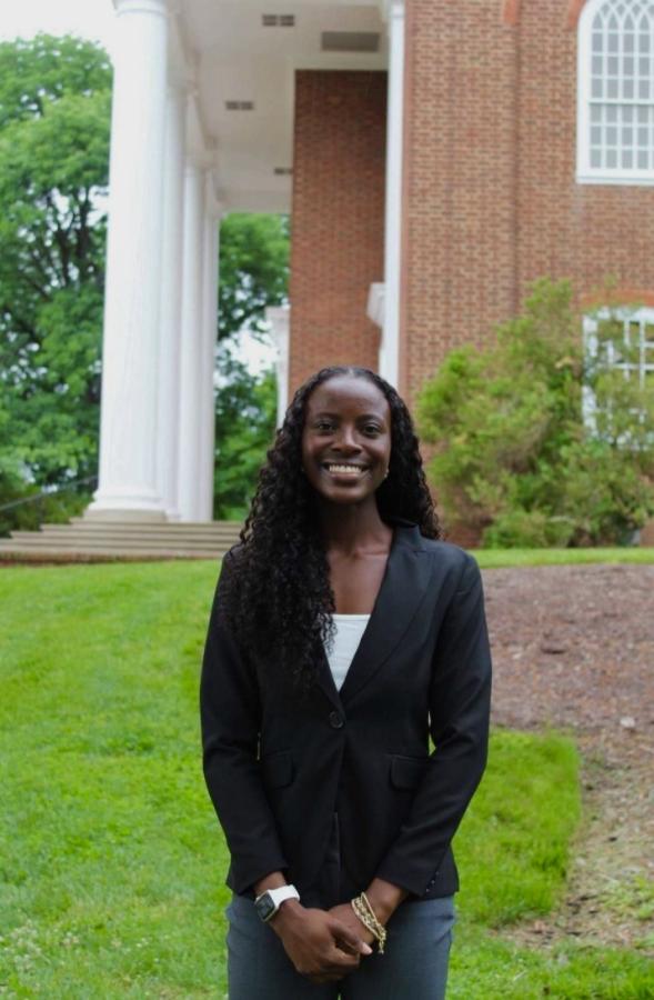 Professionally dressed students stands smiling on UMD's campus in front of an iconic white pillar set against red bricks.