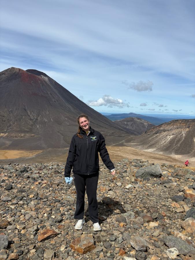 A smiling student poses in front of a vast, rocky mountainscape.