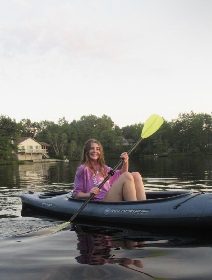A happy student paddles calm water in a kayak.